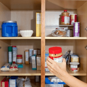 Hand grabbing peanut butter jar from a food pantry cupboard